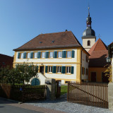 Pfarrhaus Wiesenbronn, im Hintergurnd der Turm der Heilig Kreuz-Kirche